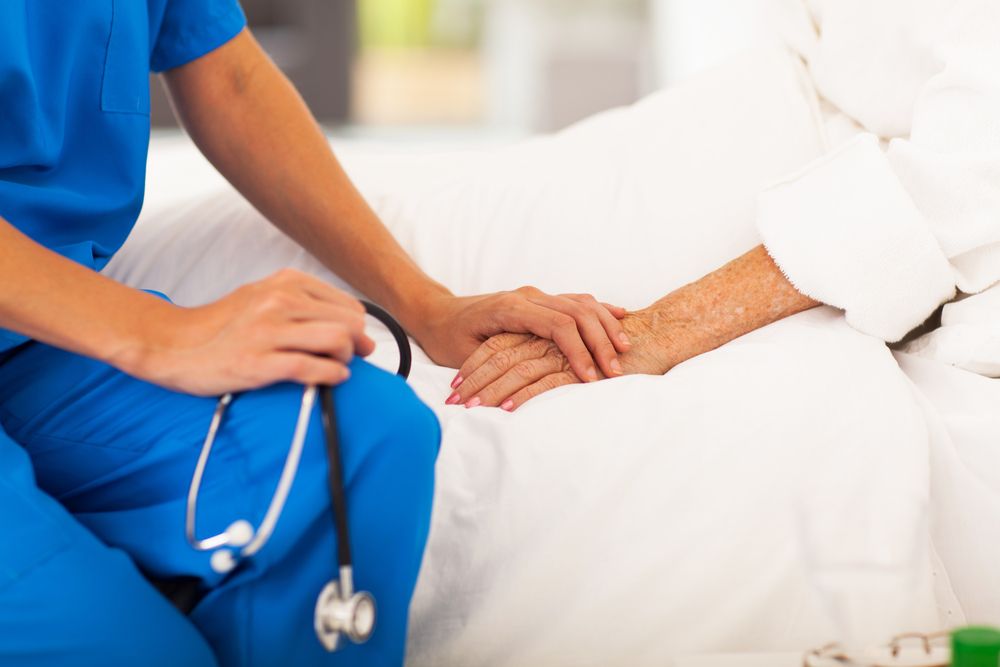 nurse holing senior patient's hands and comforting her